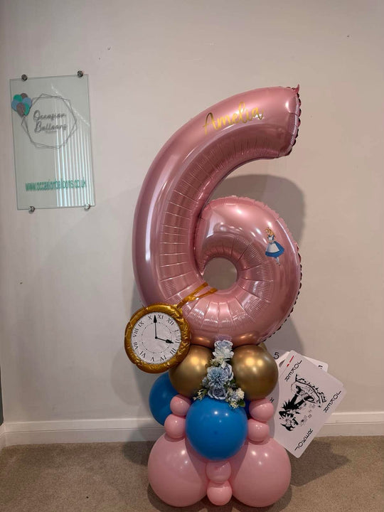 Pink number 6 balloon personalised with Amelia, featuring Alice in Wonderland details, a gold pocket watch, playing cards and a pink, blue and gold base.