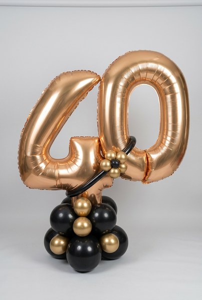 Gold 40 foil number balloons on a black and gold balloon base, finished with a black balloon band and a small gold balloon flower.