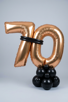 Gold 70 foil number balloons joined with black balloon bands on a freestanding black balloon base.