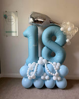 Blue 18 foil balloons personalised with Leah, topped with a silver birthday bottle balloon and clear bubbles, on a blue and white balloon base.