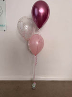 Bouquet of three helium balloons featuring a clear pink confetti balloon, a pink balloon and a metallic berry balloon with ribbons and a weight.