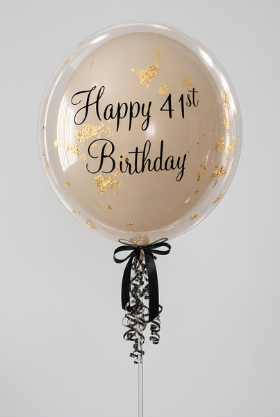 Clear bubble balloon with a neutral inner balloon, gold flake detailing, black Happy 41st Birthday wording and black bow and ribbons.