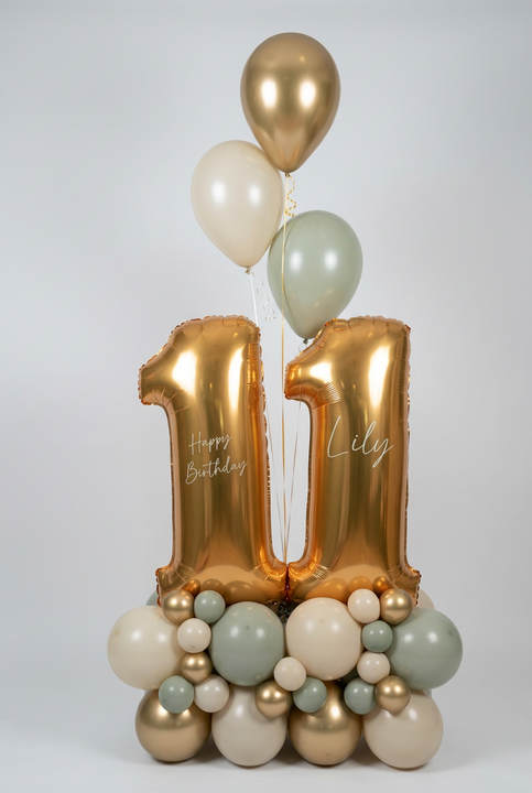 Gold number 11 balloons personalised with Lily and Happy Birthday, on a cream, grey and gold base with three matching helium balloons above.