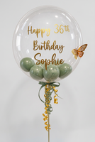 Clear bubble balloon with sage green mini balloons, gold Happy 36th Birthday Sophie wording, a gold butterfly and coordinating ribbons.