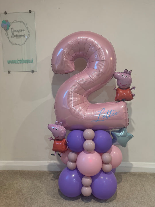 A custom balloon decoration featuring a large metallic pink number 2 balloon with the name 'Lettie' written on it, supported by a cluster of pink, purple, and lavender balloons, including Peppa Pig character balloons and a silver star balloon.