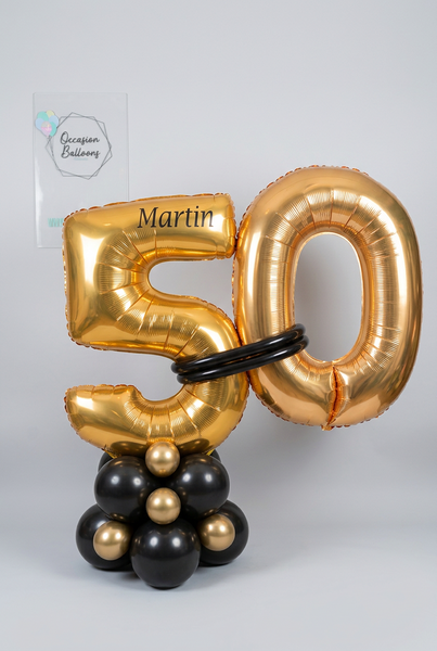 Gold 50 foil number balloons personalised with Martin, joined with black balloon bands on a black and gold balloon base.