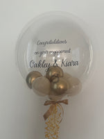 Celebrate an engagement with a personalised bubble balloon featuring the couple’s names and your chosen colours. Portland collection and local delivery. C

Image alt text: Clear engagement bubble balloon with gold and cream mini balloons, black wording for Oakley and Kiara, a ring detail and gold ribbons.