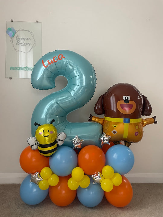 Blue number 2 balloon personalised with Luca, alongside Duggee and bee foil balloons on a blue, orange and yellow base with silver stars