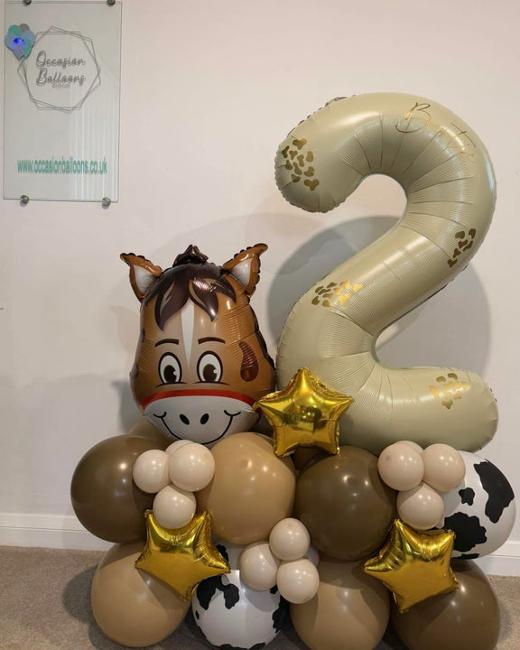 Personalised cream number 2 balloon beside a horse foil balloon, on a brown, beige, cream and cow-print base with gold stars.