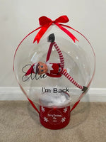 Clear personalised “I’m Back” balloon with a red elf suspended inside, finished with a red bow, ribbons and a personalised Christmas container.