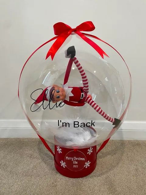 Clear personalised “I’m Back” balloon with a red elf suspended inside, finished with a red bow, ribbons and a personalised Christmas container.