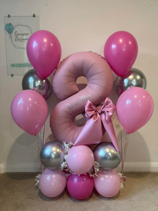 Pink number 8 balloon personalised with Rosie-Mae, with a satin bow, flowers, pink and silver balloon base and two matching helium bouquets.