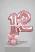 Metallic pink number 12 balloons personalised with Marley, joined by a pale pink balloon bow on a pink and white balloon base.
