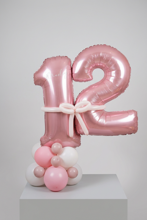 Metallic pink number 12 balloons personalised with Marley, joined by a pale pink balloon bow on a pink and white balloon base.