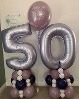 Lilac number 50 balloons on mauve, deep purple and white towers, with a personalised 24-inch birthday bubble balloon between them.