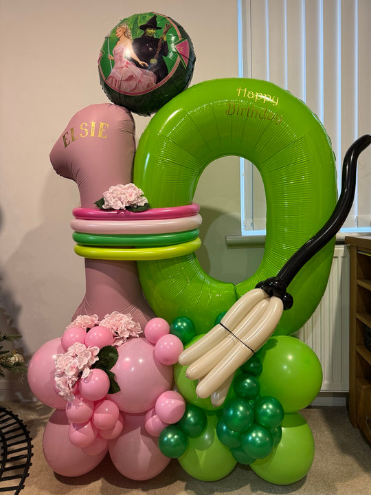 Pink and green number 10 balloons personalised with Elsie, featuring a Wicked character balloon, pink flowers and a sculpted balloon broomstick.