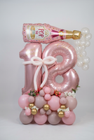 Pink 18 number balloons with gold personalisation, a white balloon bow, champagne bottle and clear balloon bubbles above a floral pink and gold base.
