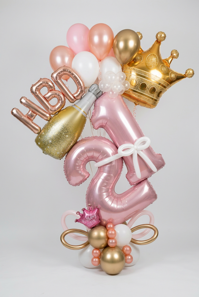  Pink 21 foil balloons with a white bow, gold crown, champagne bottle, rose gold HBD lettering and coordinating pink, white and gold balloons.