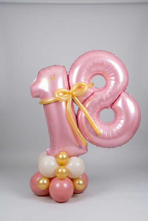  Personalised pink 18 foil number balloons with a gold balloon bow on a pink, cream and gold balloon base.