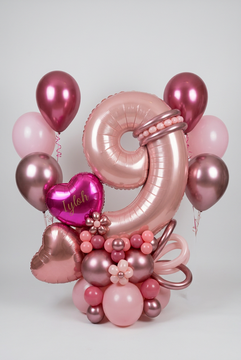 Pink number 9 balloon with personalised heart, rose gold heart, balloon flowers and a pink and berry base, beside two matching helium bouquets.