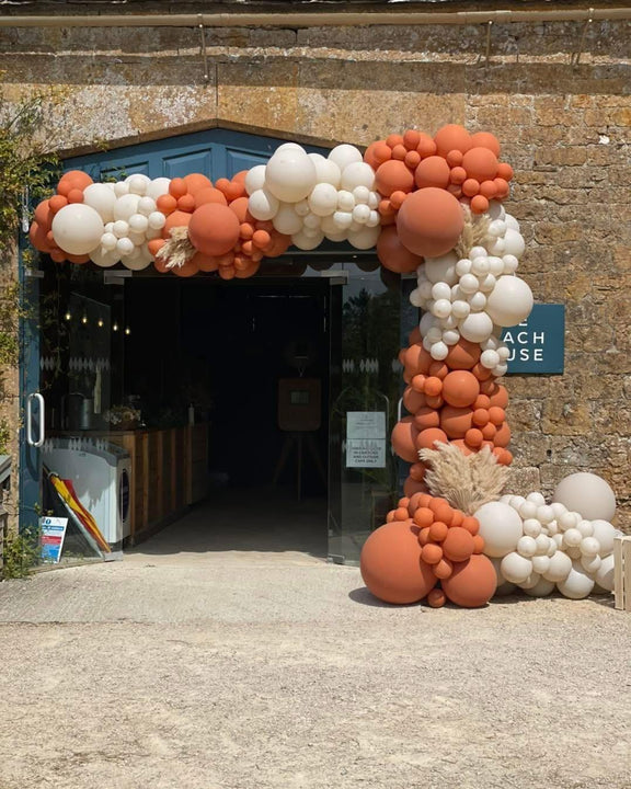  Terracotta and cream balloon garland with pampas details sweeping across a stone venue doorway and down one side.