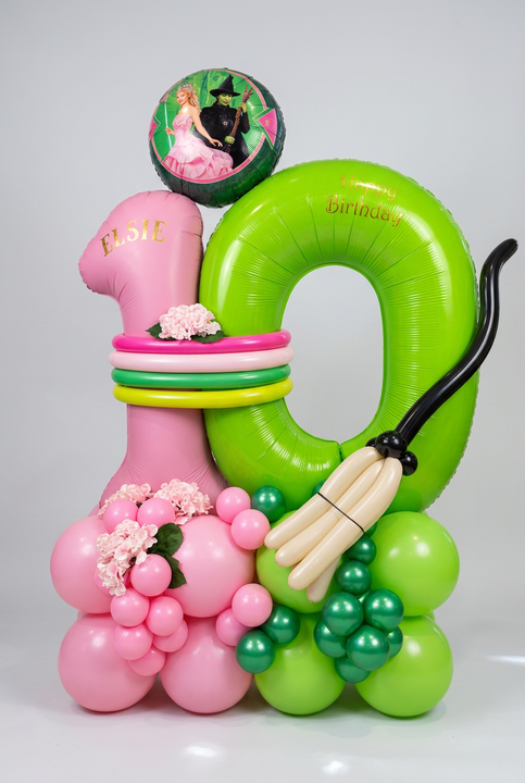 Pink and green number 10 balloons personalised with Elsie, featuring a Wicked character balloon, pink flowers and a sculpted balloon broomstick.