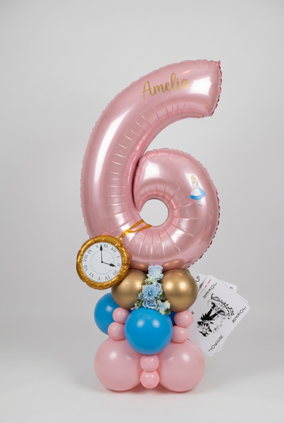 Pink number 6 balloon personalised with Amelia, featuring Alice in Wonderland details, a gold pocket watch, playing cards and a pink, blue and gold base.
