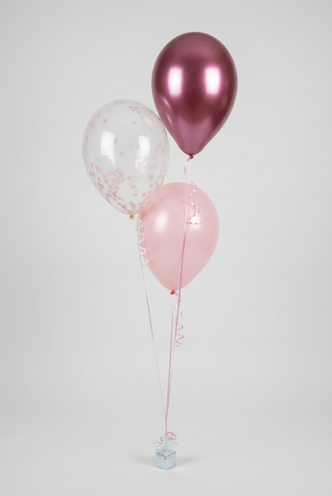 Bouquet of three helium balloons featuring a clear pink confetti balloon, a pink balloon and a metallic berry balloon with ribbons and a weight.