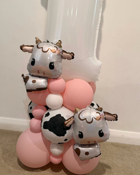 White number 1 balloon personalised with Mia-Mae in pink, with two cow foil balloons and a pink, white and cow-print balloon base.