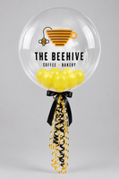 Clear bubble balloon printed with The Beehive Coffee Bakery logo, filled with yellow balloons and finished with black and yellow ribbons.