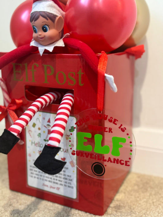 Red Elf Post box topped with red and gold balloons, featuring a seated Christmas elf, candy cane, red bow and elf surveillance sign.