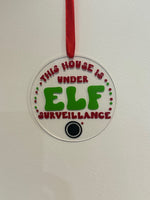 Decorative tag with 'This house is under elf surveillance' text on a white background